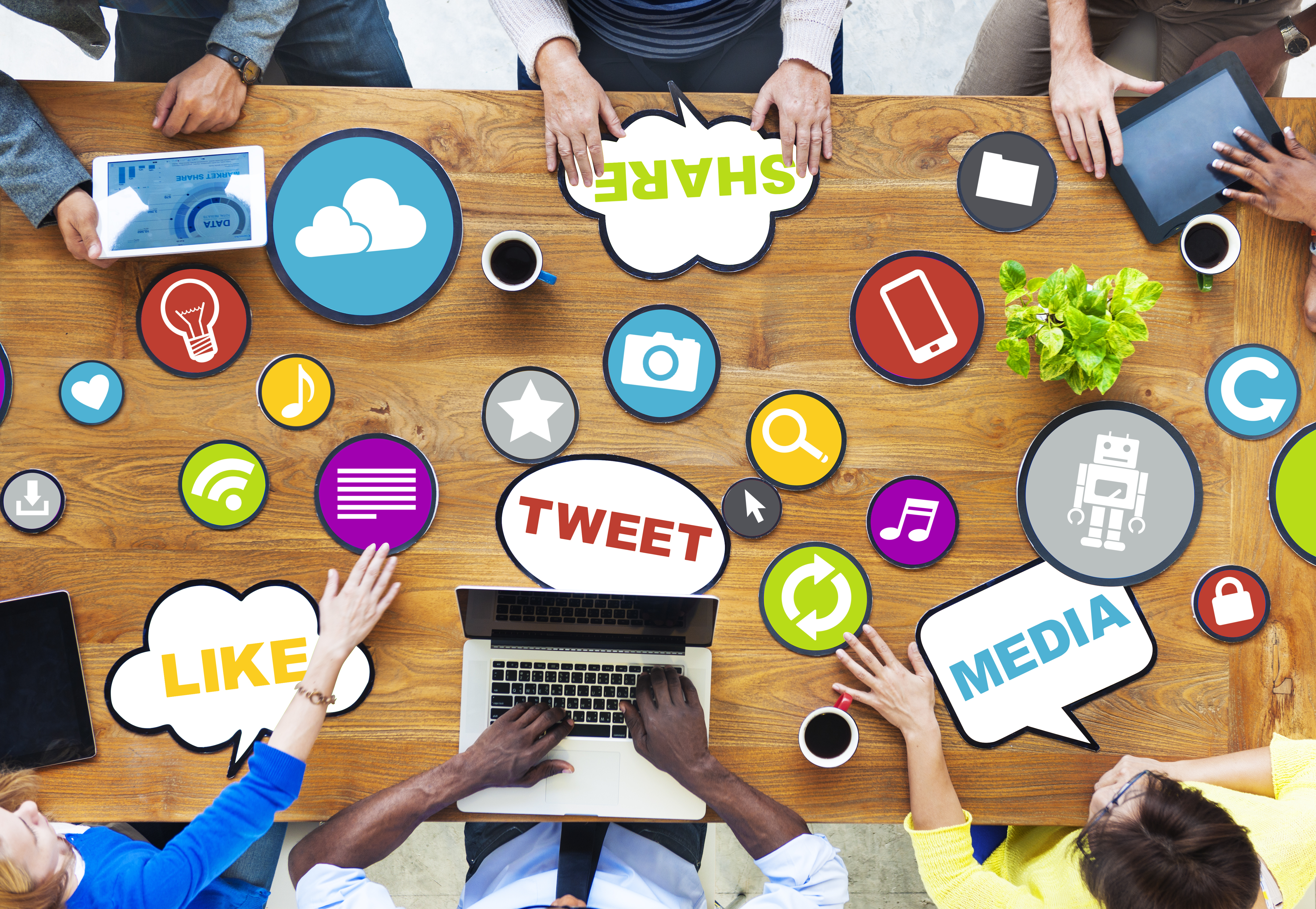 aerial view of six people working together at a desk covered in social media related icons